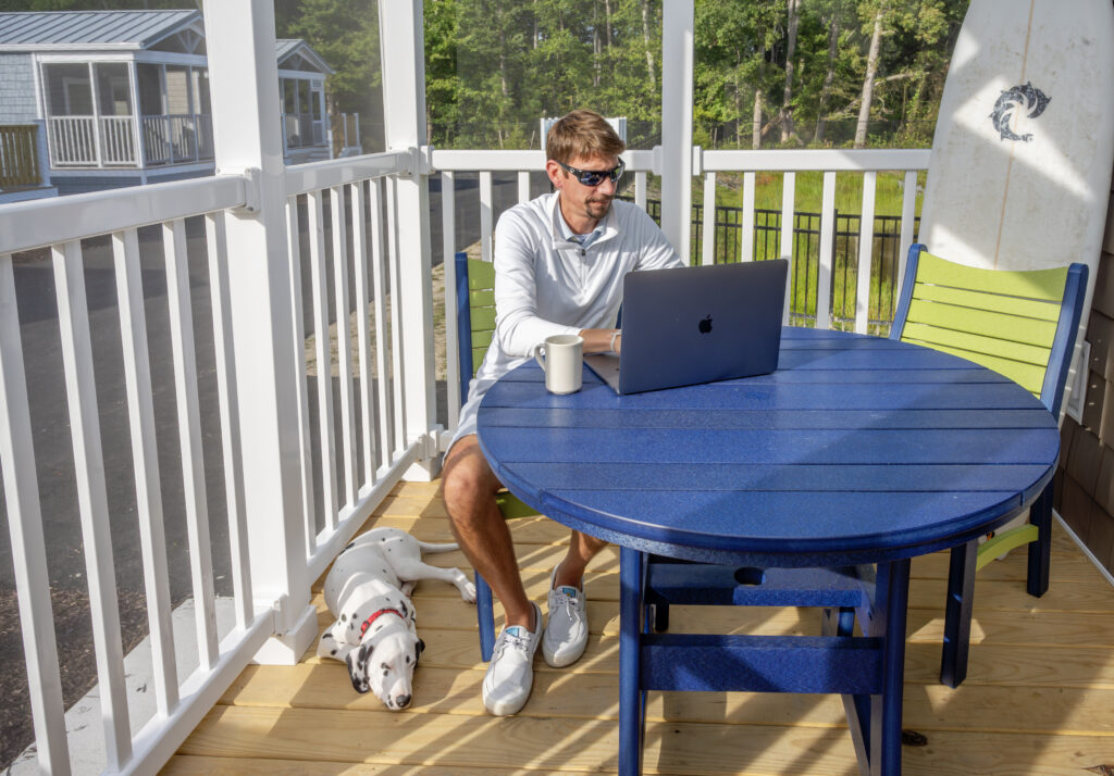 Guest enjoying screened in front porch, sitting at table working with dog laying by his feet