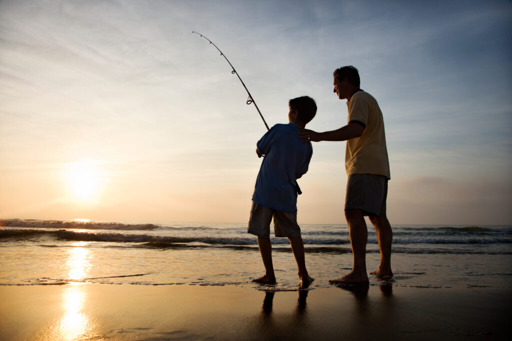 Man and young boy fishing in surf